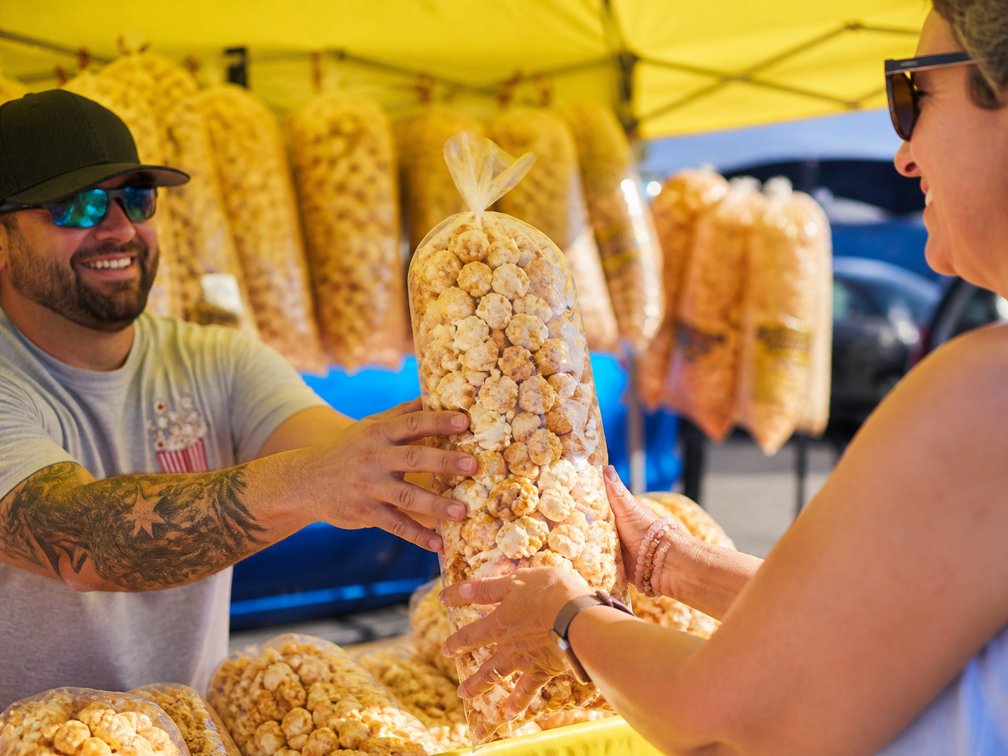 A smiling customer receiving a fresh bag of kettle corn at the yellow tent