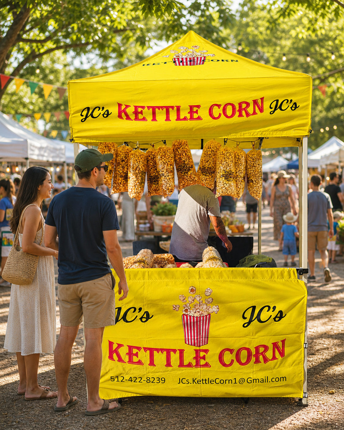 JC's yellow kettle corn tent glowing at a leafy farmers market